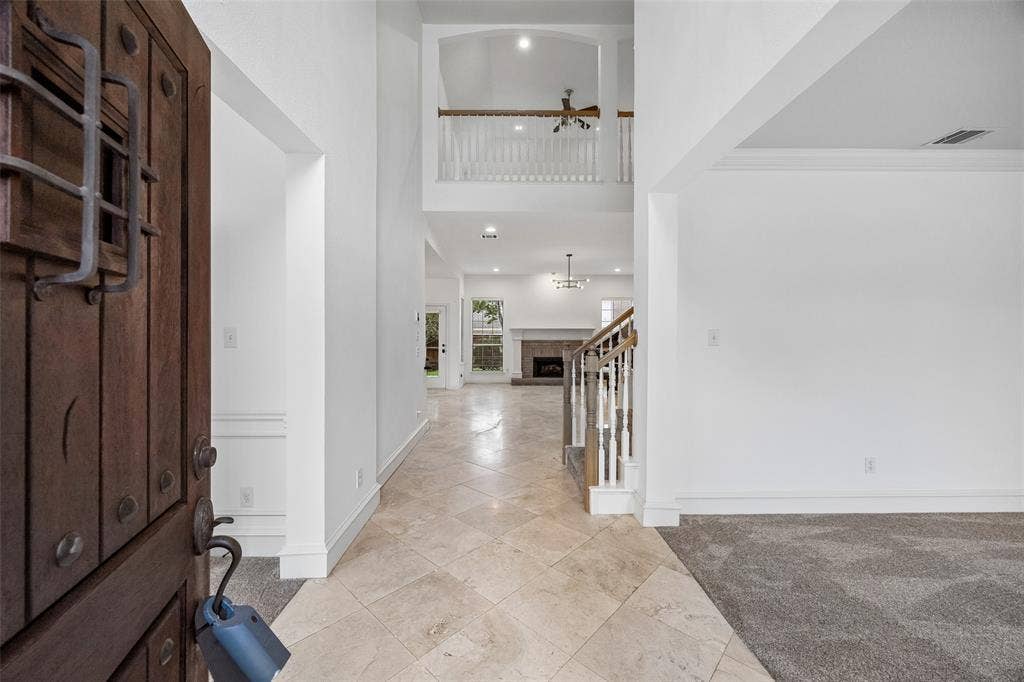2701 Oates Drive, Plano, TX 75093 Grand entryway featuring a custom wood door with iron detailing, high ceilings, a prominent staircase with white balusters, and a spacious living area with a fireplace visible beyond