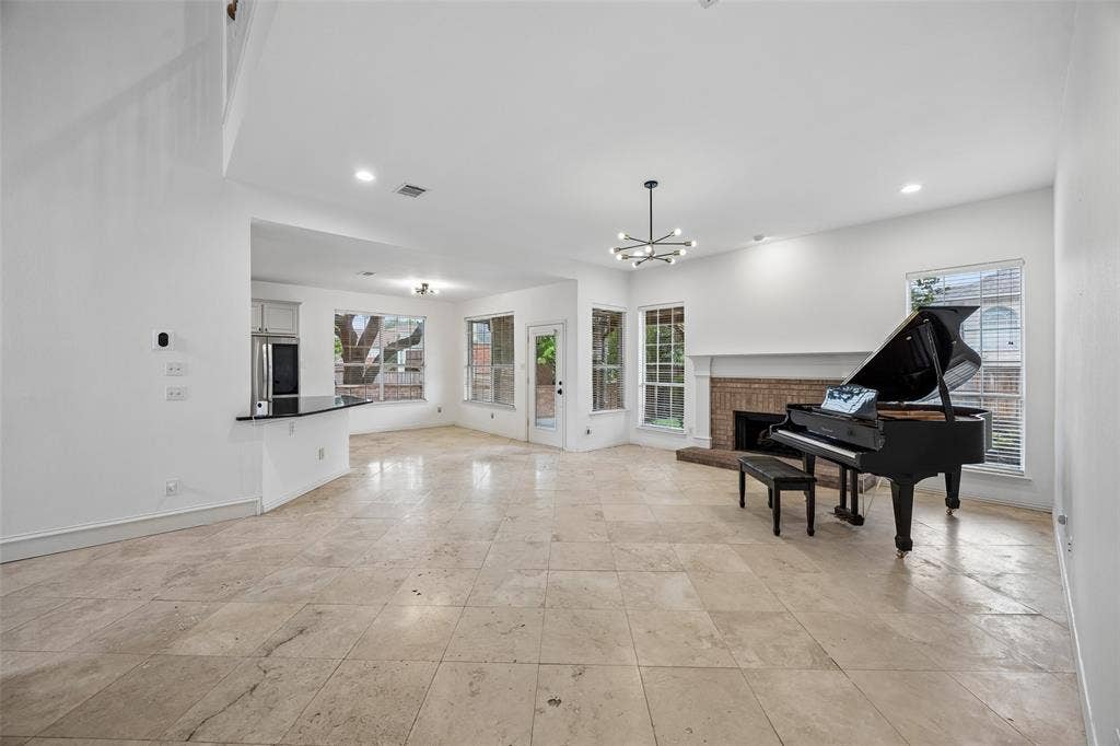 2701 Oates Drive, Plano, TX 75093 Spacious open-concept living area featuring a fireplace with a brick surround, white mantle, multiple windows, and a built-in breakfast bar with a dark countertop