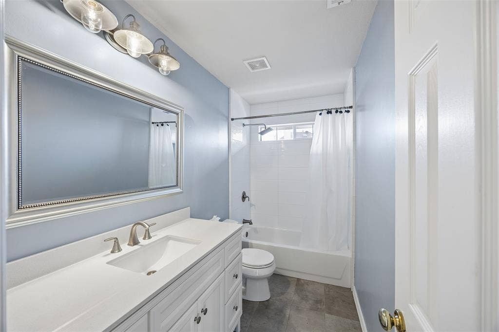 2701 Oates Drive, Plano, TX 75093 Bathroom featuring a white vanity with an integrated sink and brushed nickel faucet, framed rectangular mirror, and three-light fixture