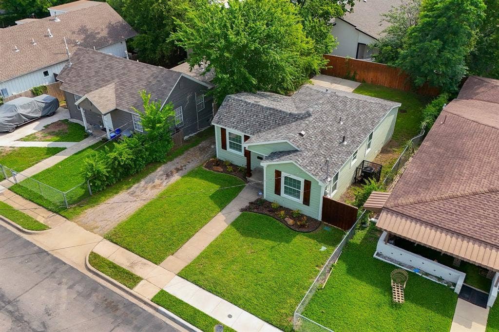 414 Avenue I, Dallas, TX 75203 Light green siding home featuring a dark shingle roof, brown window shutters, and a well-maintained front lawn with established landscaping