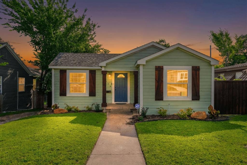 414 Avenue I, Dallas, TX 75203 Light green siding exterior with a dark blue entry door, wood shutters, and a covered porch