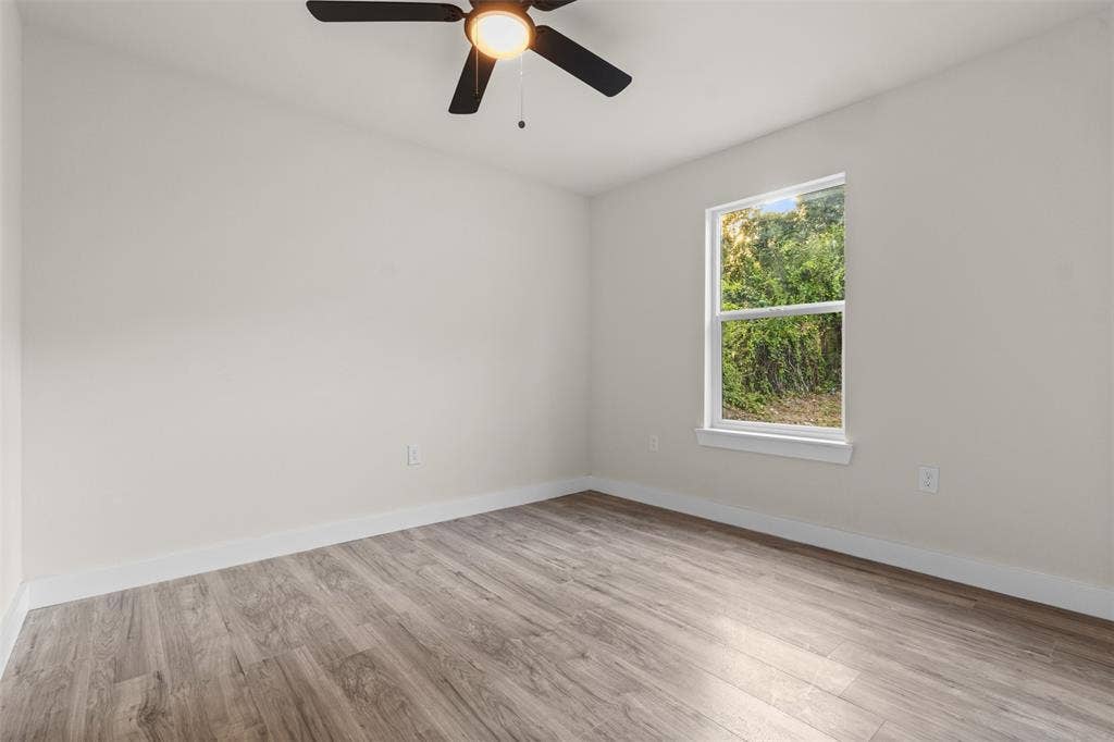 1507 E Waco Avenue, Dallas, TX 75216 Neutral wall finishes with wood-finish flooring, a ceiling fan with integrated lighting, and a single window with white trim