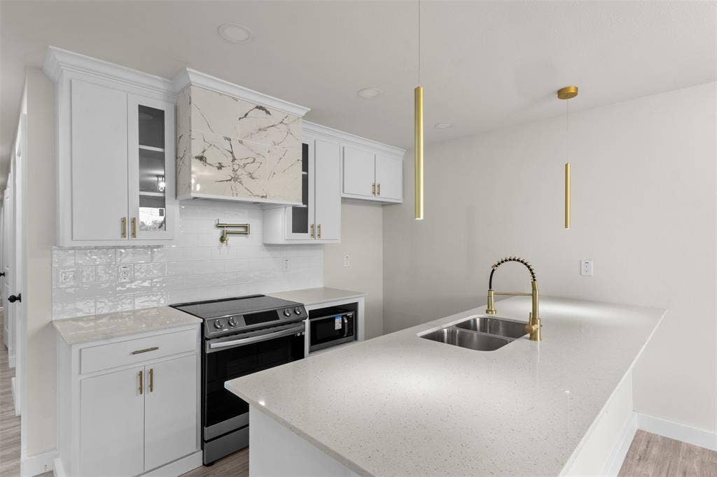 1507 E Waco Avenue, Dallas, TX 75216 Modern kitchen featuring white cabinetry with gold-tone hardware, a striking marble-patterned range hood, white subway tile backsplash, and light-colored countertops
