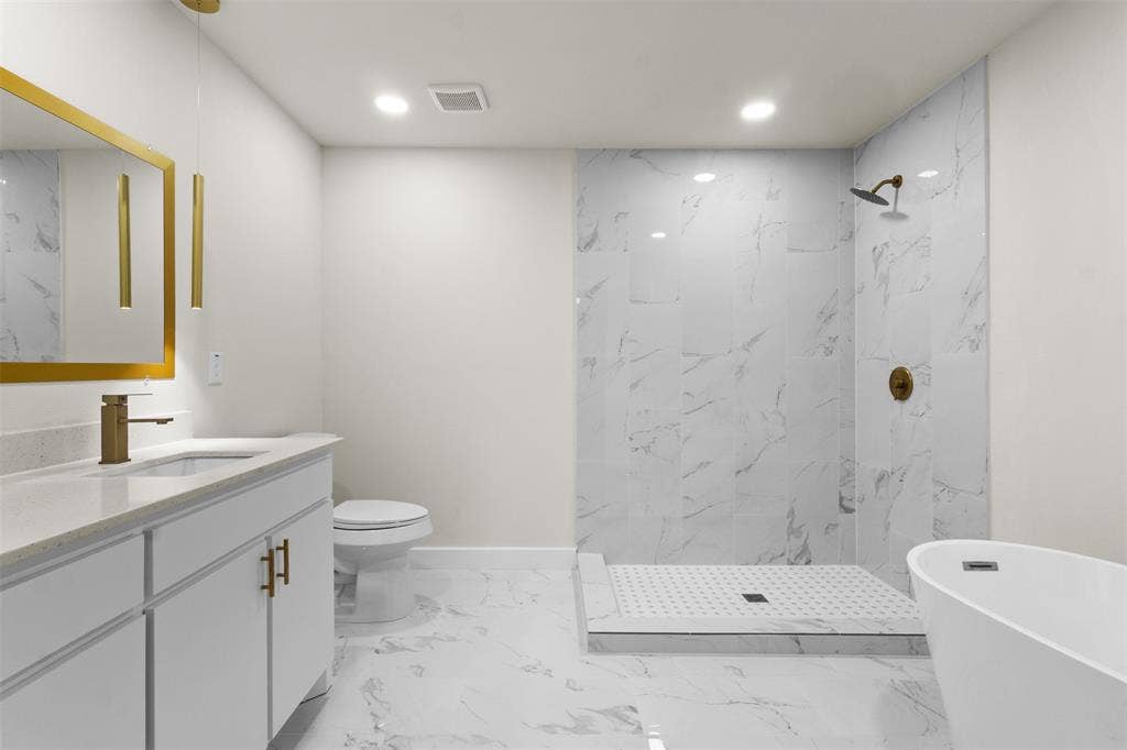 1507 E Waco Avenue, Dallas, TX 75216 Bathroom featuring a free-standing soaking tub, walk-in shower with large format tile, white vanity with integrated sink, quartz-finish countertop, and gold-finish fixtures