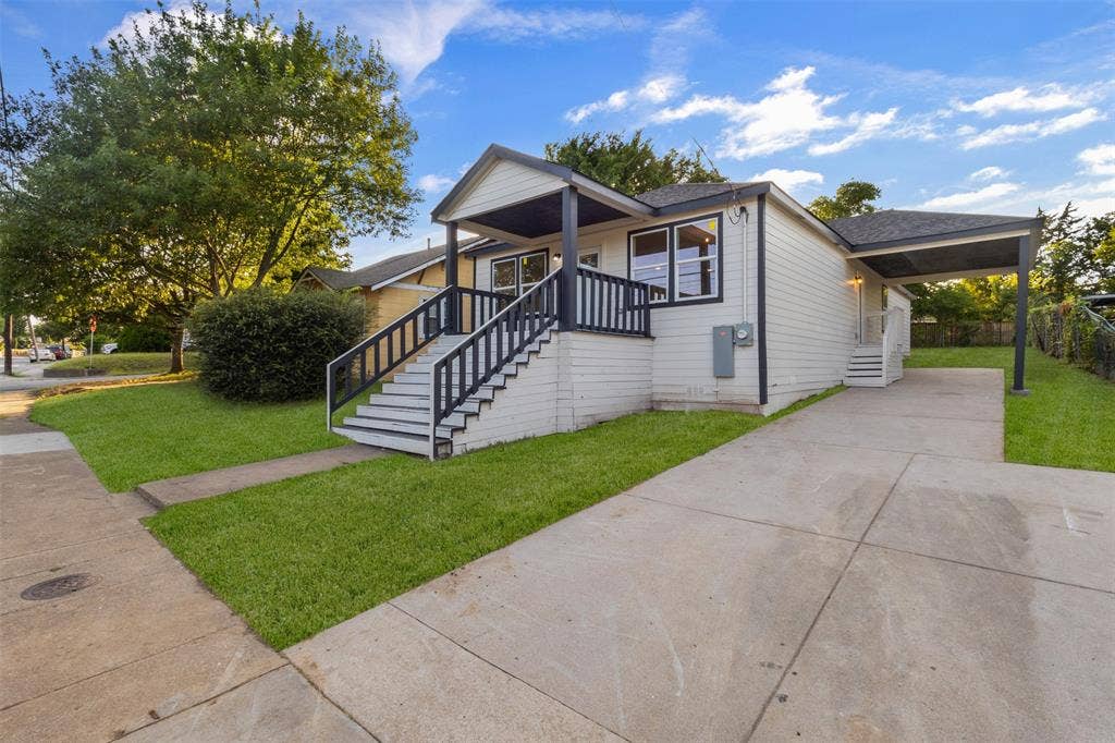 1507 E Waco Avenue, Dallas, TX 75216 Ranch-style residence featuring white siding, a covered front porch with black railings, a paved driveway, and a covered carport
