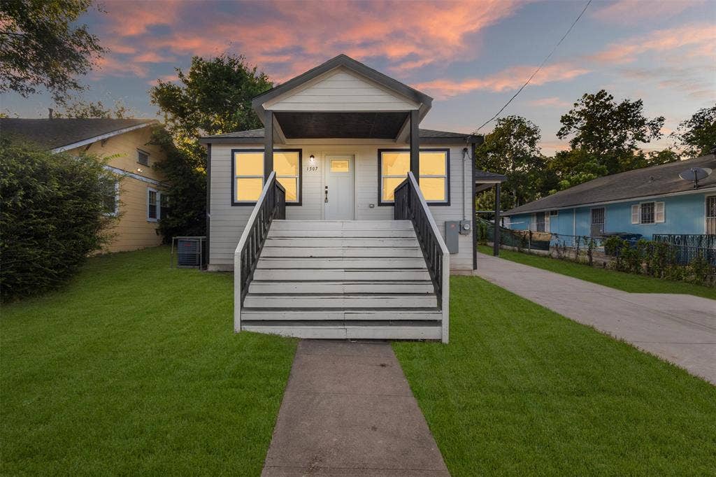 1507 E Waco Avenue, Dallas, TX 75216 Exterior featuring a central entrance with a covered porch, white siding, dark trim windows, and a manicured lawn
