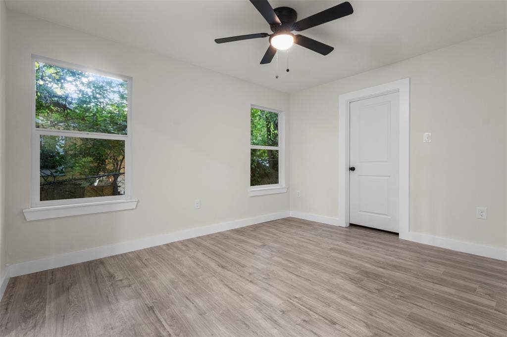 1507 E Waco Avenue, Dallas, TX 75216 Room featuring two windows, wood-finish flooring, a ceiling fan with light fixture, and a paneled interior door with dark hardware
