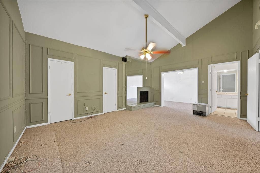 12574 Burninglog Lane, Dallas, TX 75243 Spacious living area featuring a vaulted ceiling with exposed beams, decorative wall paneling, and a corner fireplace