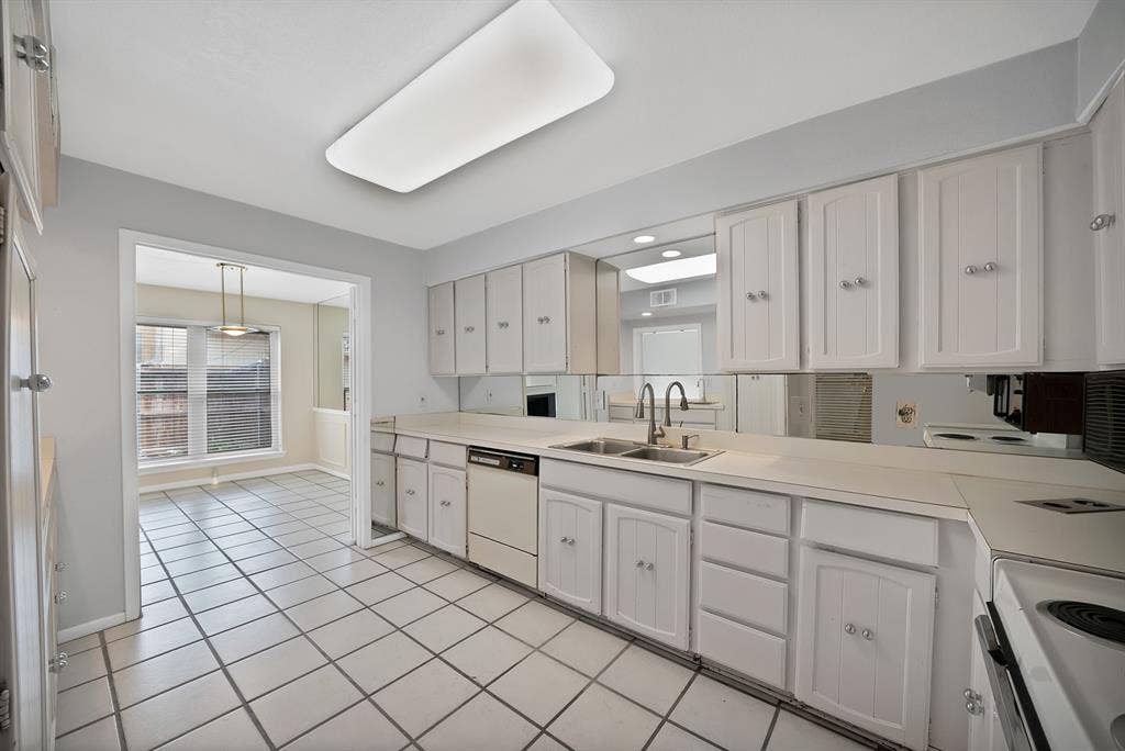 12574 Burninglog Lane, Dallas, TX 75243 Kitchen featuring white paneled cabinetry, light-toned countertops, a mirrored backsplash, and a double basin sink with a gooseneck faucet