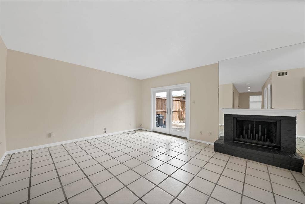 12574 Burninglog Lane, Dallas, TX 75243 Spacious room with large ceramic tile flooring, a prominent black brick fireplace with a white mantel, and mirrored wall accents