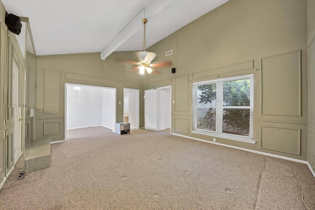 12574 Burninglog Lane, Dallas, TX 75243 Spacious interior room featuring vaulted ceilings with exposed beams, wainscoting paneling, and an overhead ceiling fan with integrated lighting
