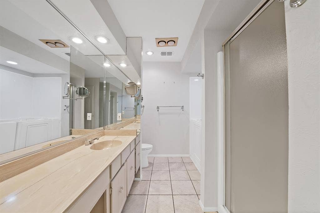 12574 Burninglog Lane, Dallas, TX 75243 Bathroom featuring a dual vanity with light-toned countertops, integrated sinks, and extensive mirror coverage