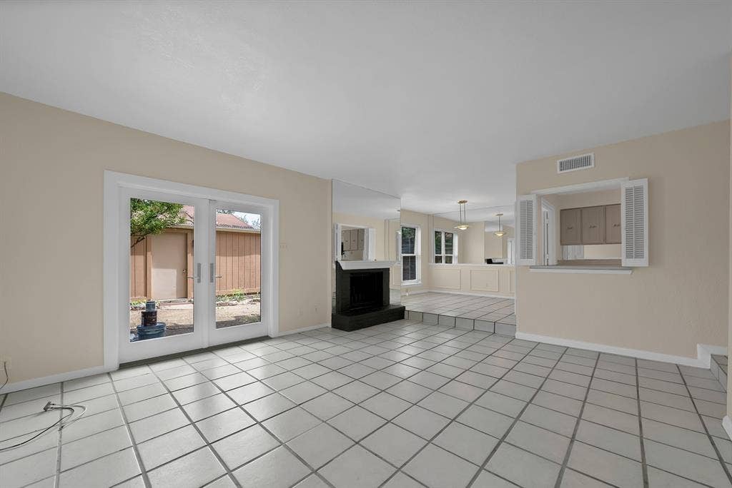 12574 Burninglog Lane, Dallas, TX 75243 Spacious interior featuring light-colored tile flooring, a black hearth and fireplace, and white-framed glass French doors