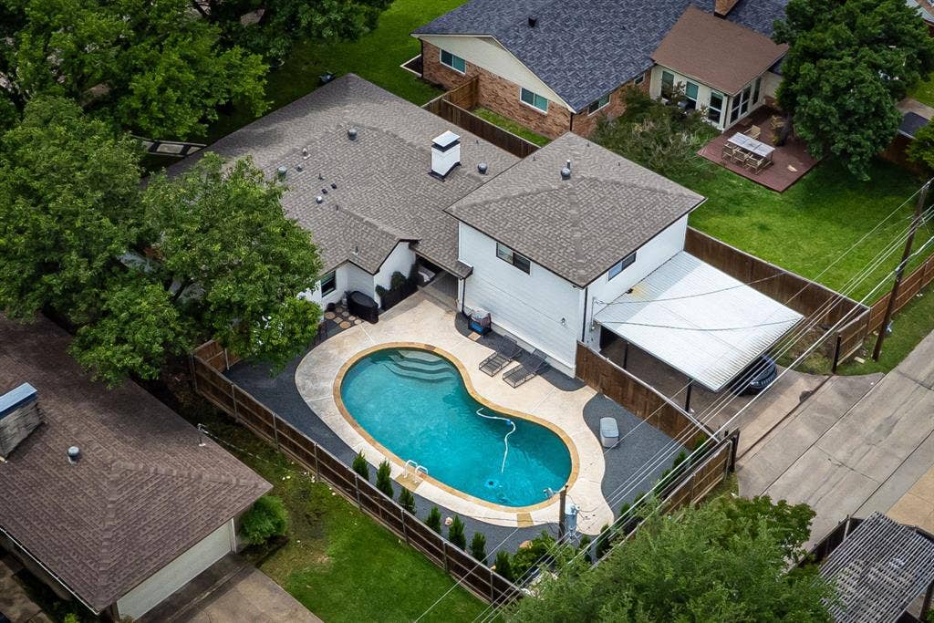 Private backyard featuring a freeform swimming pool with integrated steps, surrounding concrete decking, and perimeter fencing