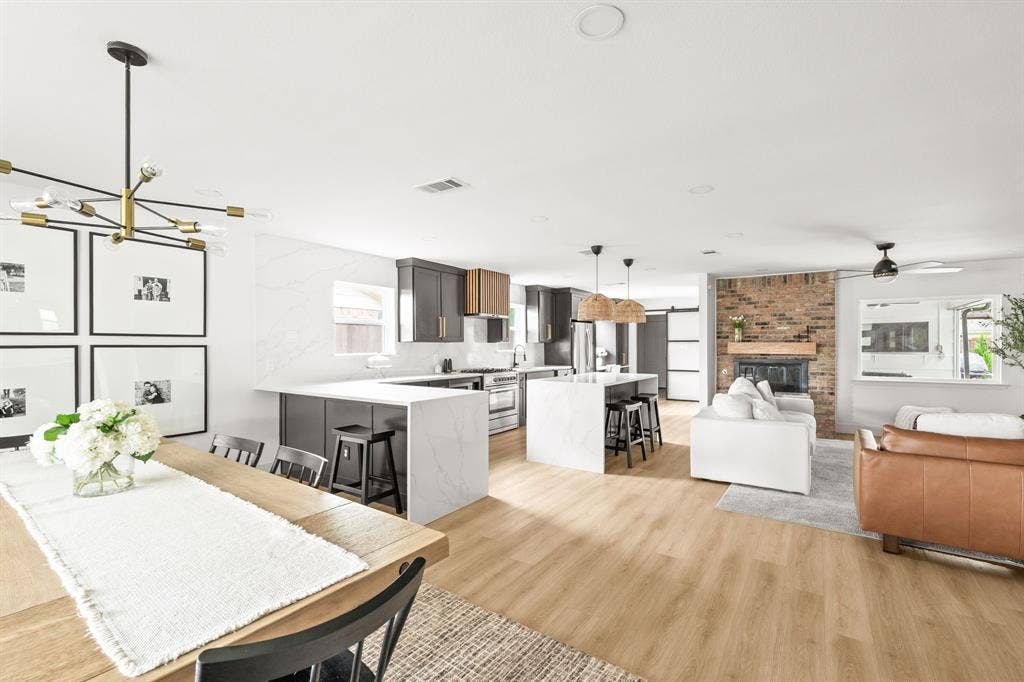 Open-concept living area featuring wood-finish flooring, a brick fireplace with a wood mantle, and recessed lighting
