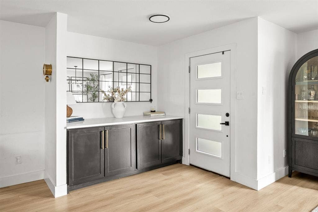 Entryway featuring a white door with frosted glass panels, a built-in dark cabinetry with gold-tone hardware and white countertop, and light wood-finish flooring