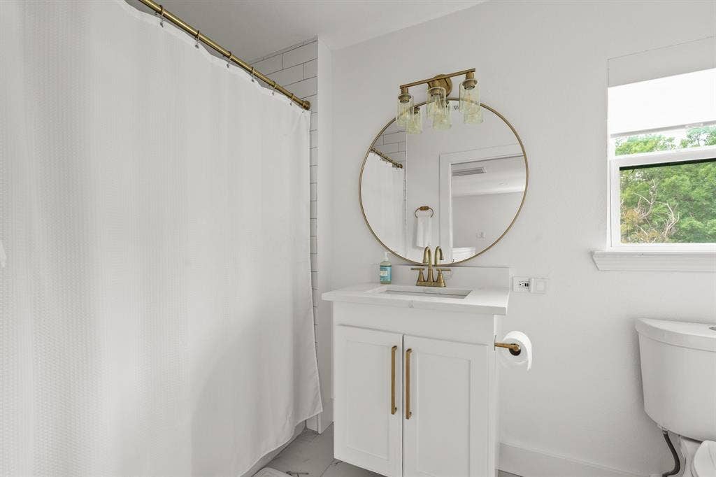 Bathroom featuring a white vanity with gold-finish hardware, a circular gold-framed mirror, and a three-light vanity fixture