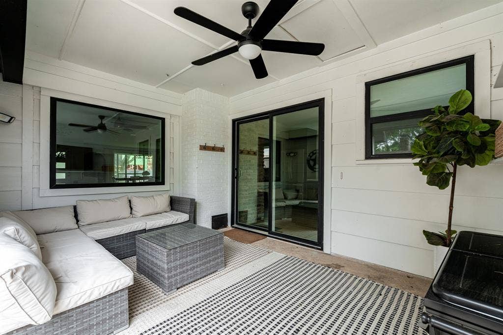 Covered patio featuring a ceiling fan, white shiplap walls, a white painted brick column, black-framed windows, and a black-framed sliding glass door