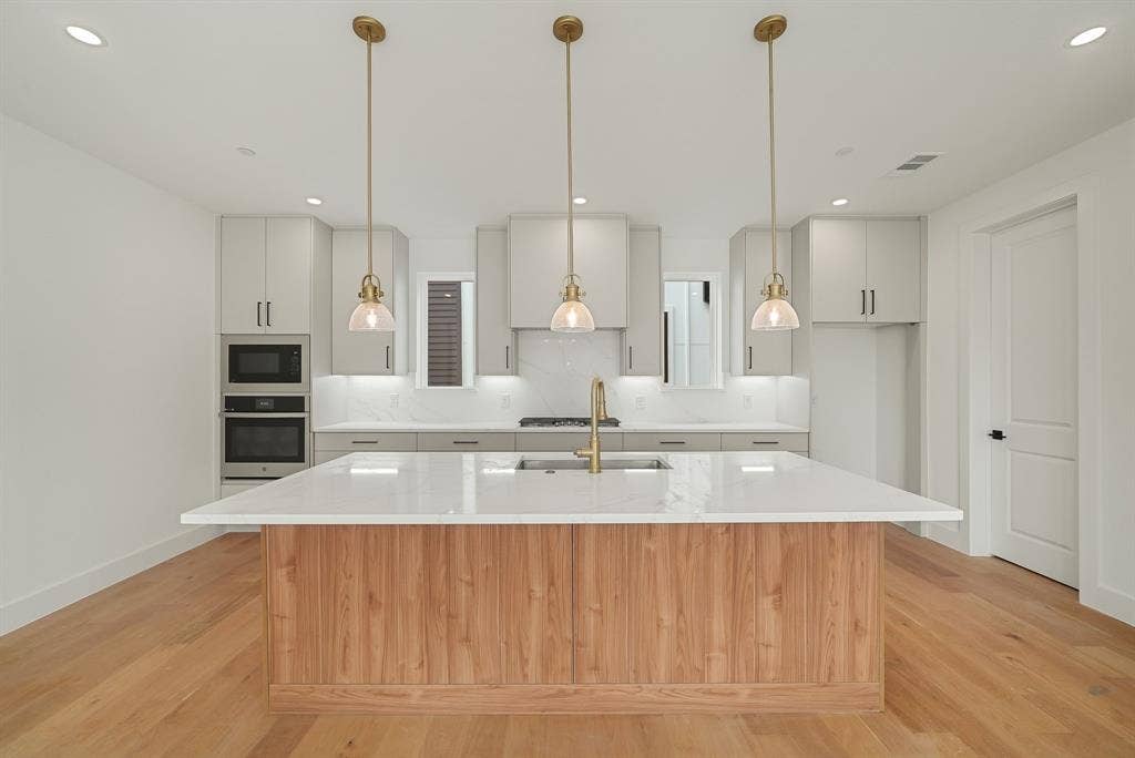4715 Manett Street, #102, Dallas, TX 75204 Kitchen featuring a wood-finish island with a white countertop, light gray cabinetry, built-in stainless steel appliances, and wood-finish flooring