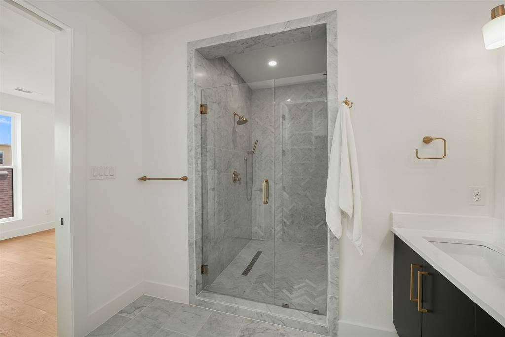 4715 Manett Street, #102, Dallas, TX 75204 Glass-enclosed shower with a rainfall showerhead, marble-style wall tiles in a herringbone pattern, coordinating marble-style floor tiles, and a linear drain