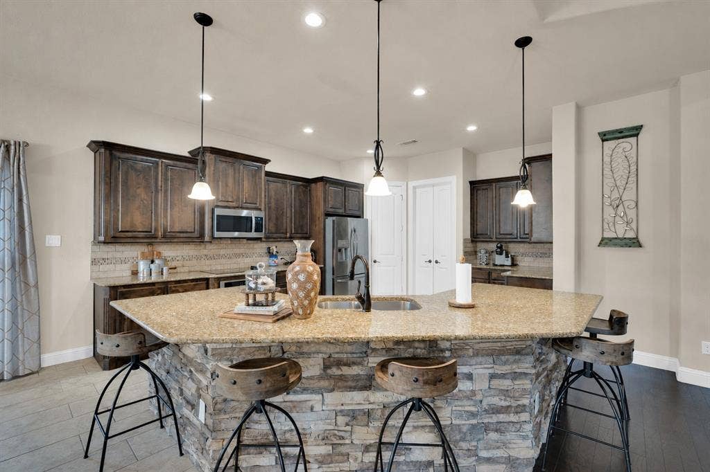 Beautiful, oversized kitchen island with stacked stone surround, featuring pendant light and beautiful cabinetry.