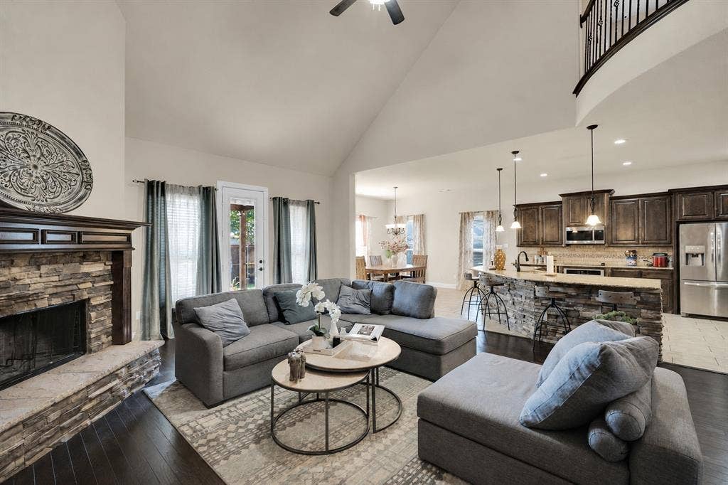 Gorgeous living room facing the kitchen, featuring hard wood floors, tall ceilings and natural light, and wood-burning fireplace with stacked stone surround.