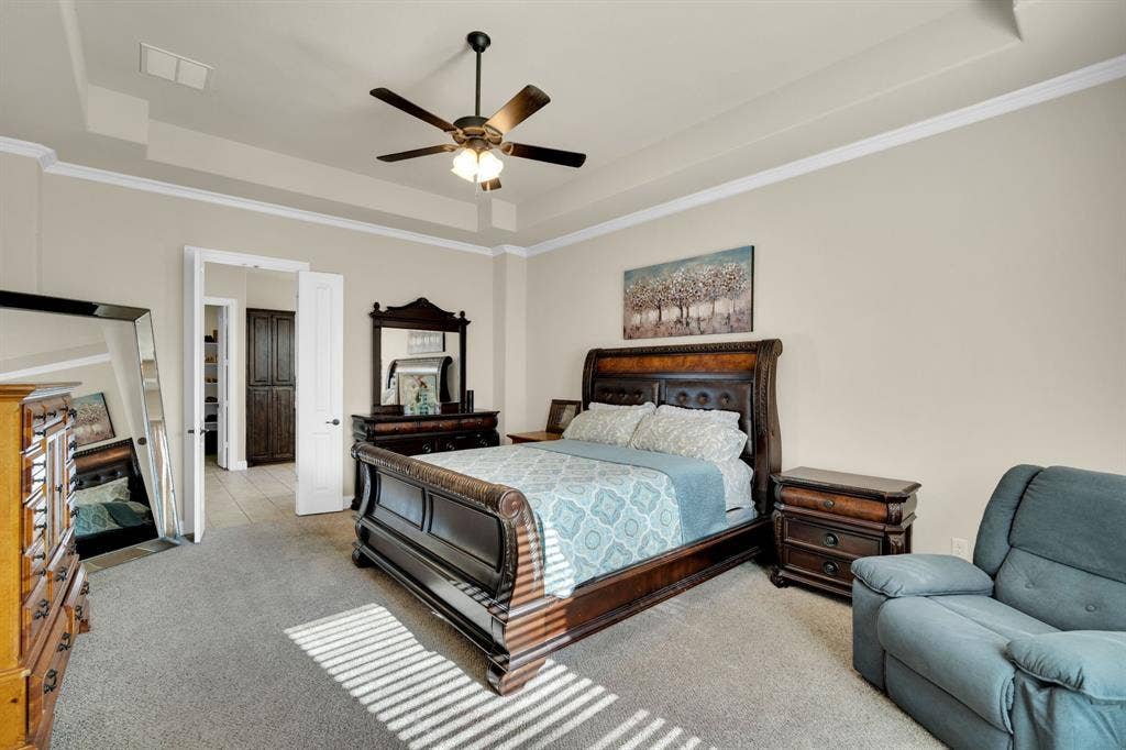 Another view of the primary bedroom facing the bathroom, and featuring the tray ceiling with crown molding. Notice the double door entry to the bathroom.