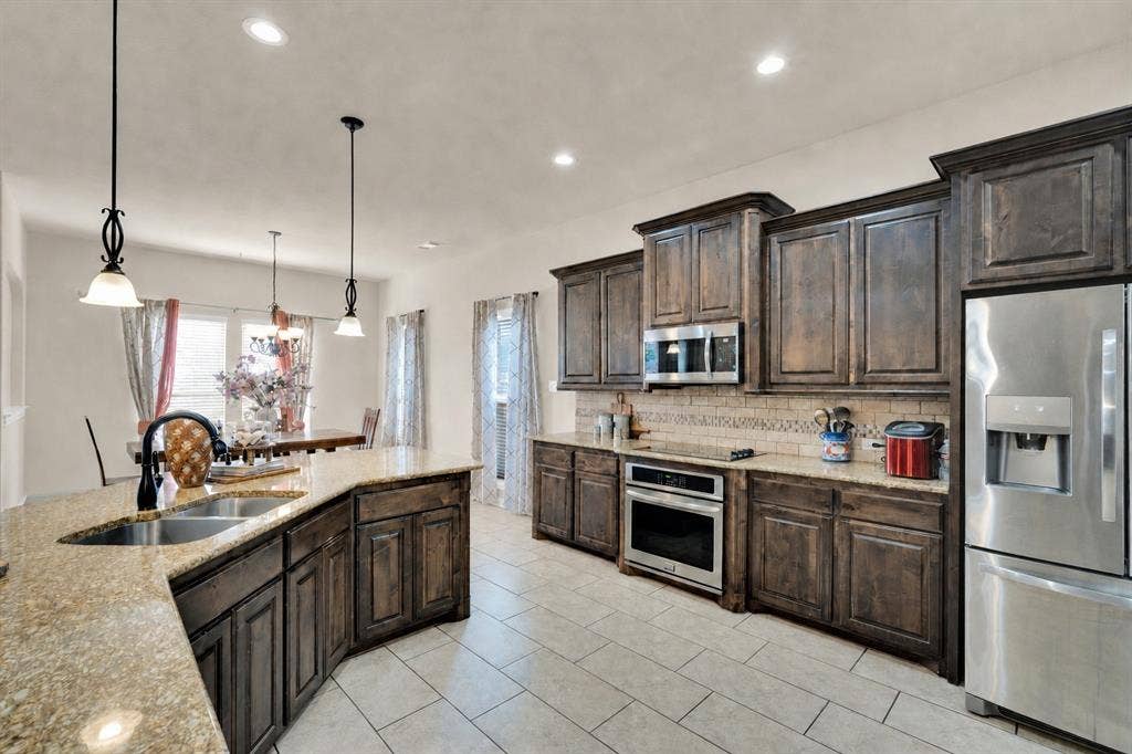 Another view of the spacious kitchen with pendant lighting, stainless steel appliances, beautiful cabinetry and tile floors.