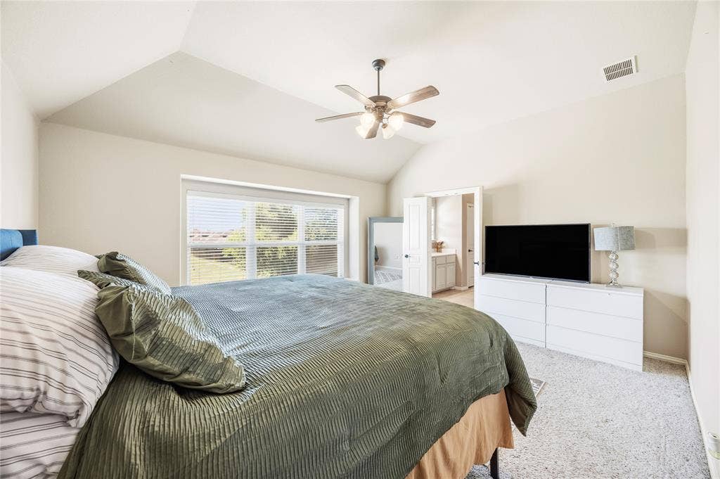 1133 Vickery Drive, DeSoto, TX 75115 2nd floor Primary bedroom two suite. Vaulted ceiling with ceiling fan, large window with blinds, light-colored carpet flooring, and an open doorway to an interior space private full bathroom.