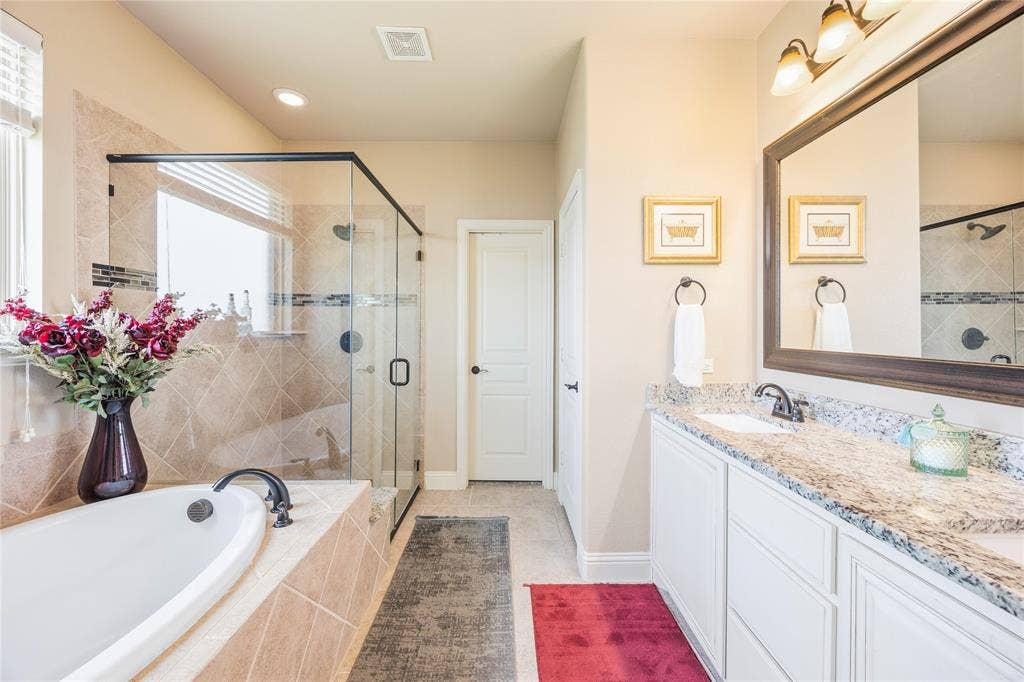 1133 Vickery Drive, DeSoto, TX 75115 Bathroom featuring a built-in soaking tub with tiled surround, a glass-enclosed shower with tiled walls and dark bronze fixtures, and a double vanity with a light-toned countertop, undermount sinks, and dark bronze faucets
