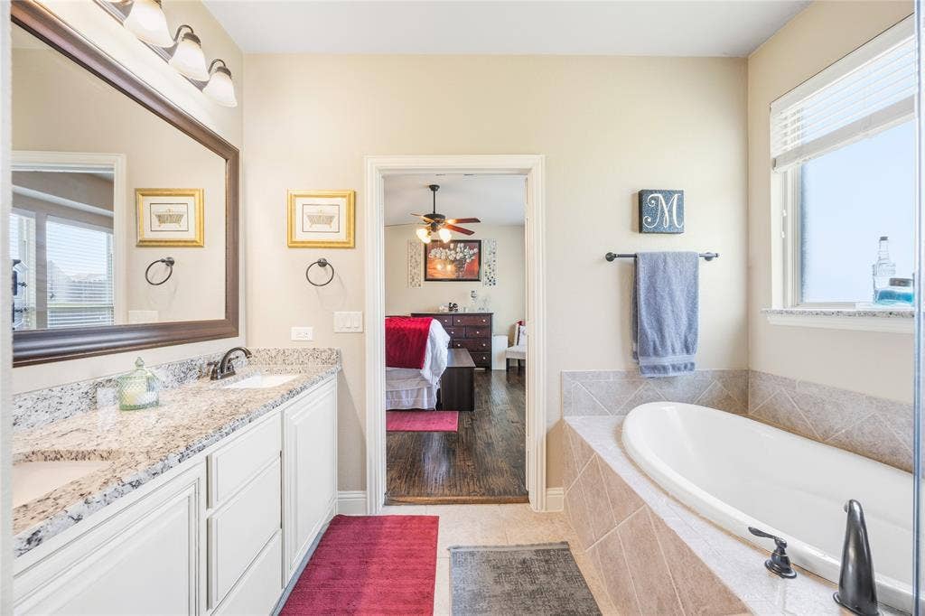 1133 Vickery Drive, DeSoto, TX 75115 Dual sink vanity with stone countertop, mounted mirror, and built-in soaking tub with tiled surround