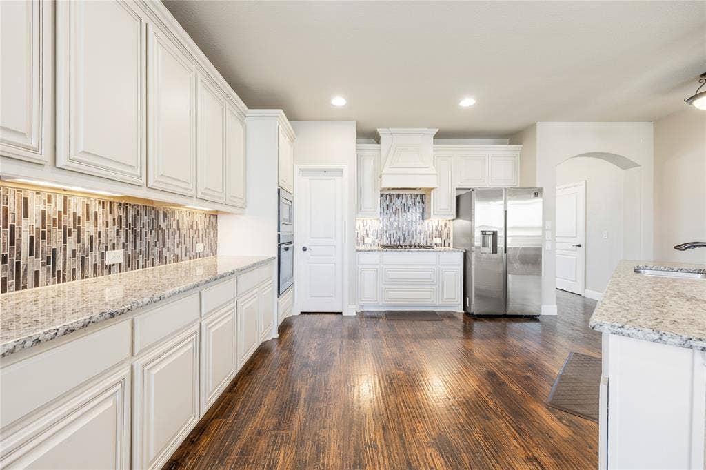 1133 Vickery Drive, DeSoto, TX 75115 Kitchen featuring wood-finish flooring, white cabinetry, speckled countertops, stainless steel appliances, and a mosaic tile backsplash