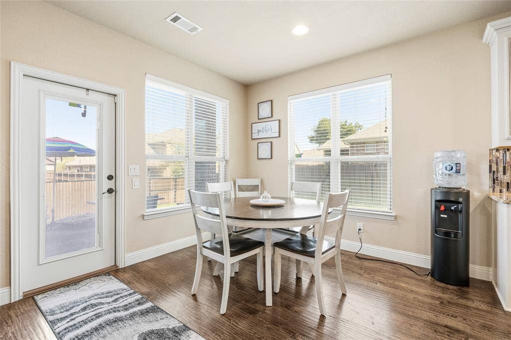 1133 Vickery Drive, DeSoto, TX 75115 Dining area featuring wood-finish flooring, two large windows with blinds, and a white door with a glass panel