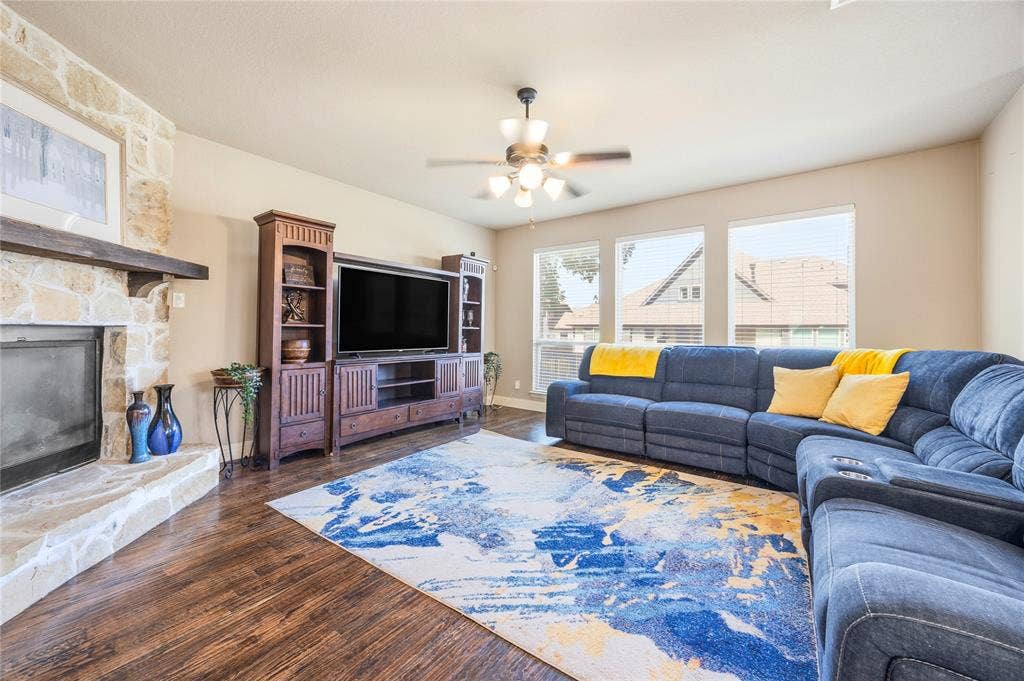 1133 Vickery Drive, DeSoto, TX 75115 Spacious living area featuring a stone fireplace with a wood mantle, wood-finish flooring, and a ceiling fan with integrated lighting