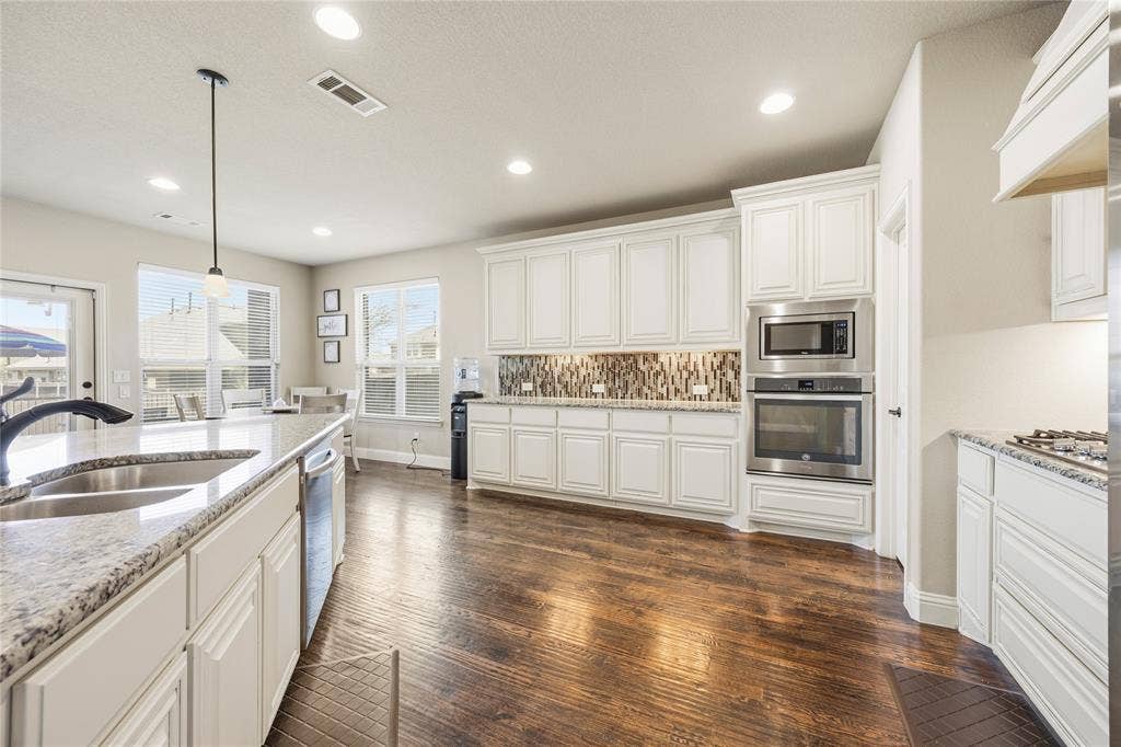 1133 Vickery Drive, DeSoto, TX 75115 Gourmet kitchen featuring white cabinetry, granite countertops, built-in stainless steel appliances, wood-finish flooring, and a decorative tile backsplash