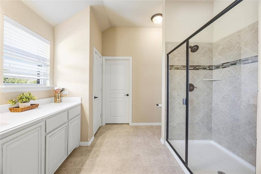 1133 Vickery Drive, DeSoto, TX 75115 Spacious 2nd floor primary bathroom featuring a glass-enclosed shower with tile surround and decorative accent band with sink and spacious countertop space.