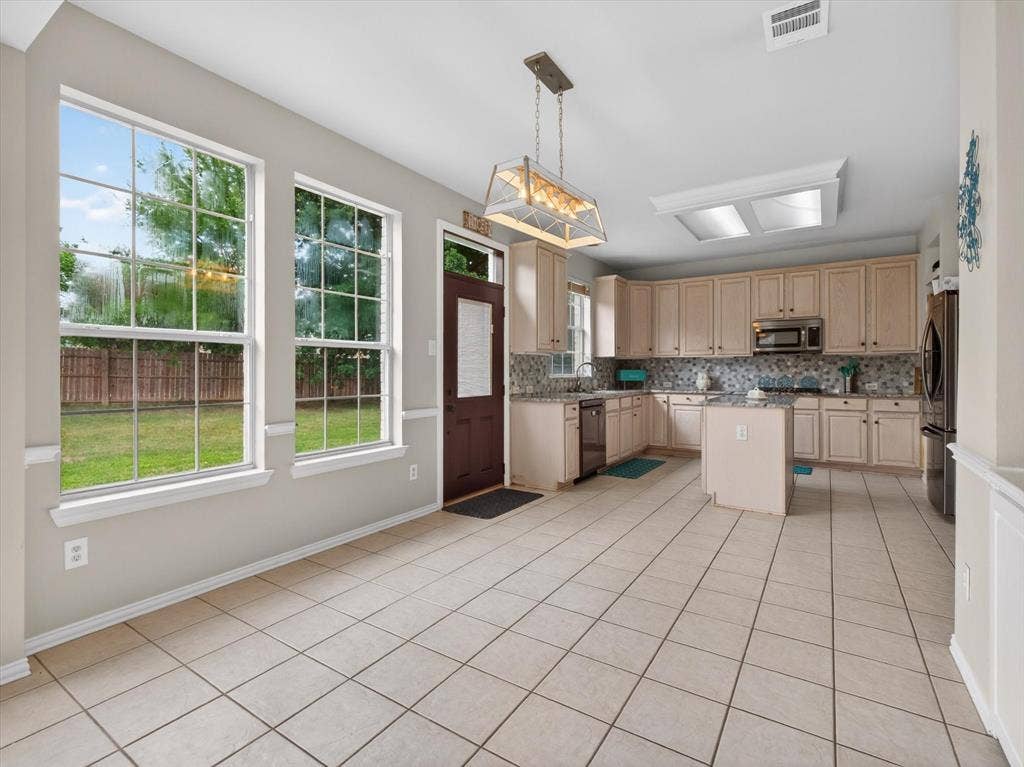 1712 Tealwood Lane, Corinth, TX 76210 Open-concept kitchen and dining area featuring tile flooring, light wood cabinetry, stone countertops, and a patterned tile backsplash