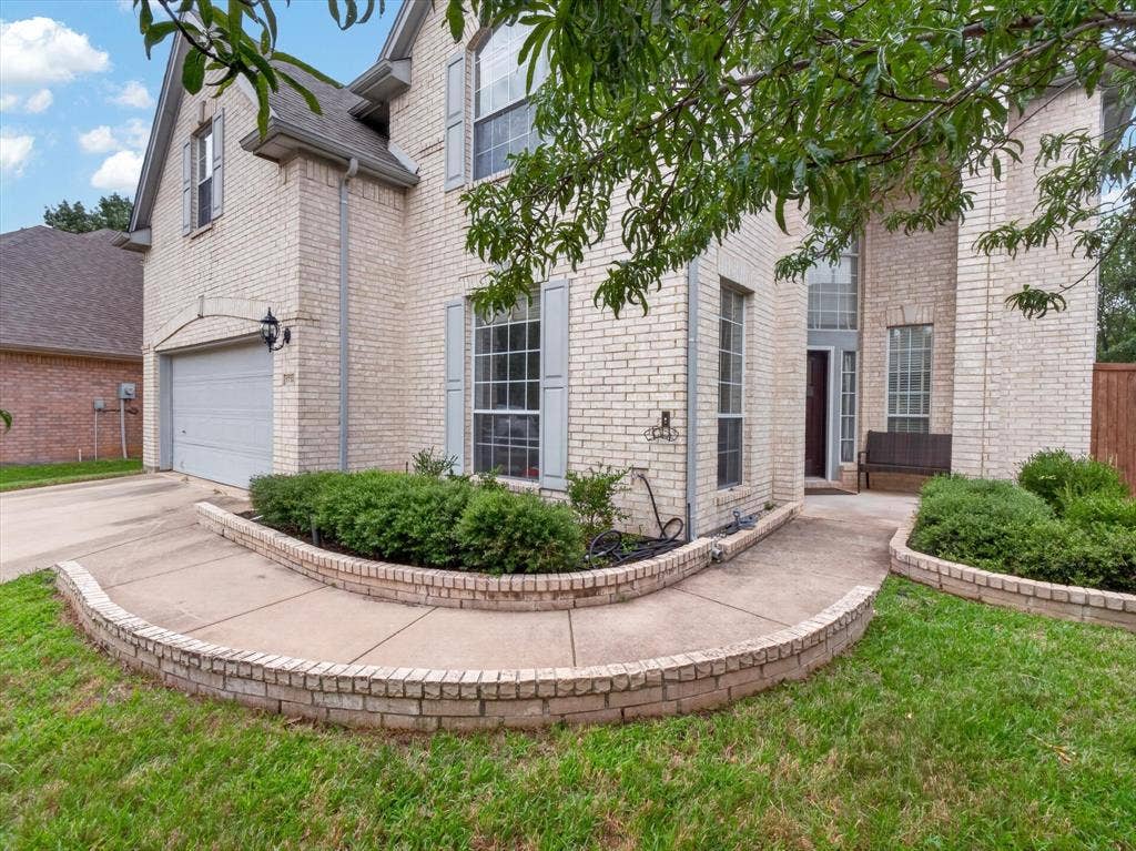 1712 Tealwood Lane, Corinth, TX 76210 Brick exterior home featuring a two-car garage, concrete driveway, and front lawn with mature trees and landscape curbing