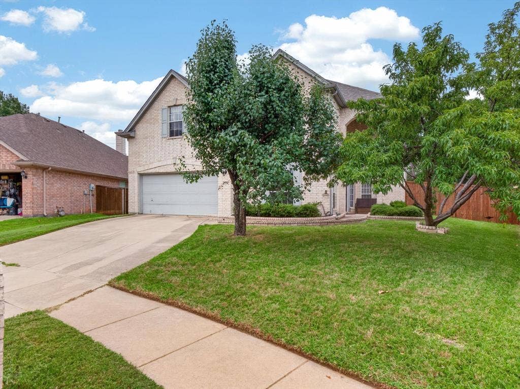 1712 Tealwood Lane, Corinth, TX 76210 Brick exterior home featuring a two-car garage, concrete driveway, and front lawn with mature trees and landscape curbing