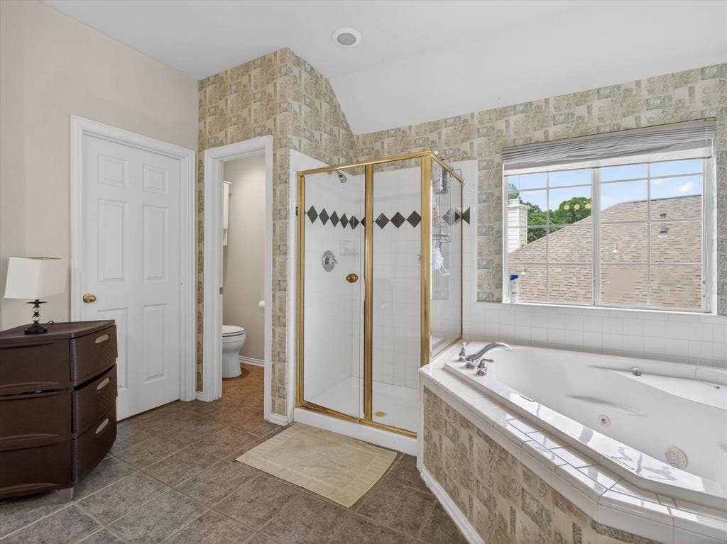 1712 Tealwood Lane, Corinth, TX 76210 Bathroom featuring a corner soaking tub with tile surround, a glass-enclosed shower with gold-tone framing, and tiled flooring