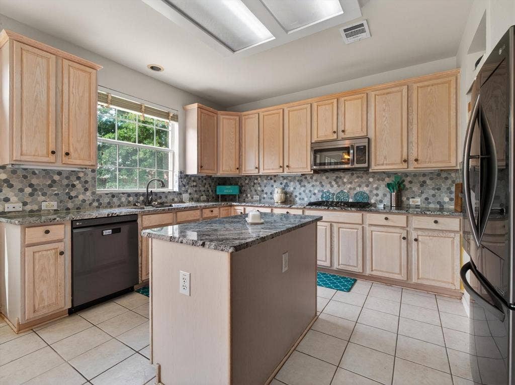 1712 Tealwood Lane, Corinth, TX 76210 Kitchen featuring a central island with a stone countertop, light wood cabinetry, mosaic tile backsplash, recessed lighting, and a window overlooking exterior greenery