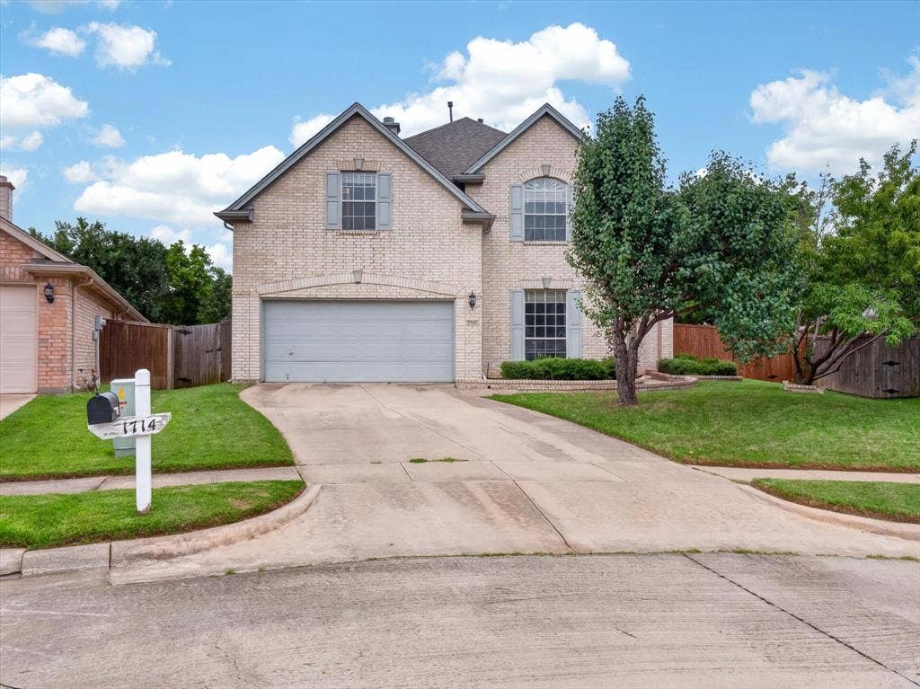 1712 Tealwood Lane, Corinth, TX 76210 Two-story brick exterior featuring a multi-car driveway, attached garage, arched window, and established landscaping