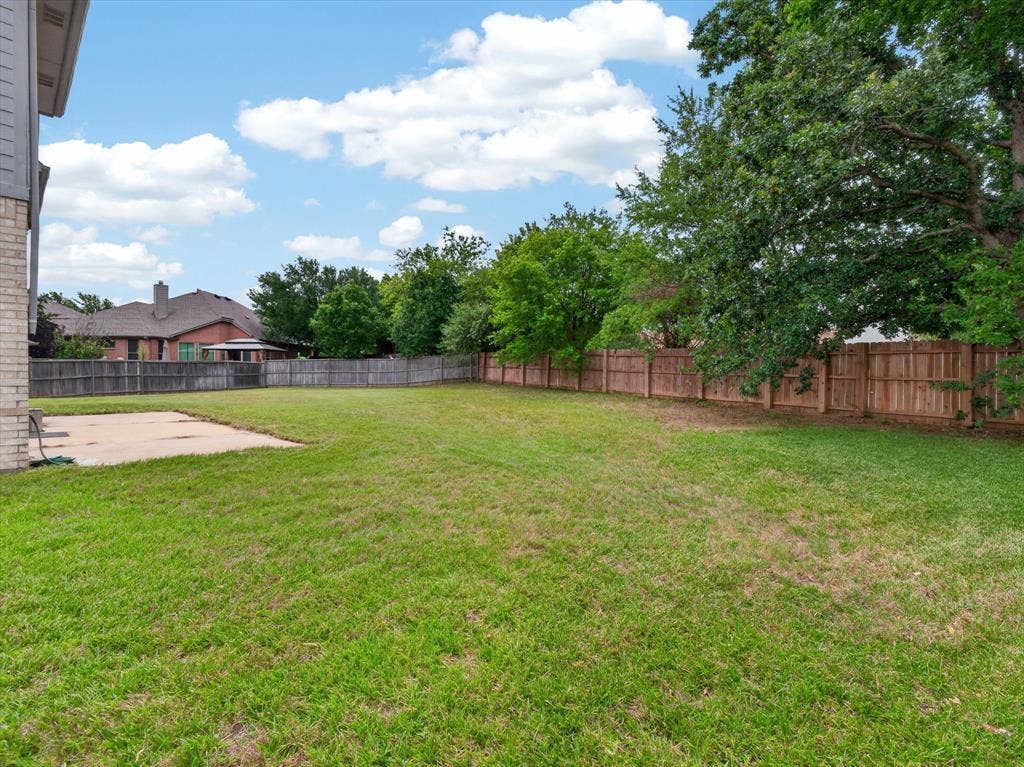 1712 Tealwood Lane, Corinth, TX 76210 Expansive grassy backyard featuring a concrete patio, mature trees, and a full perimeter fence