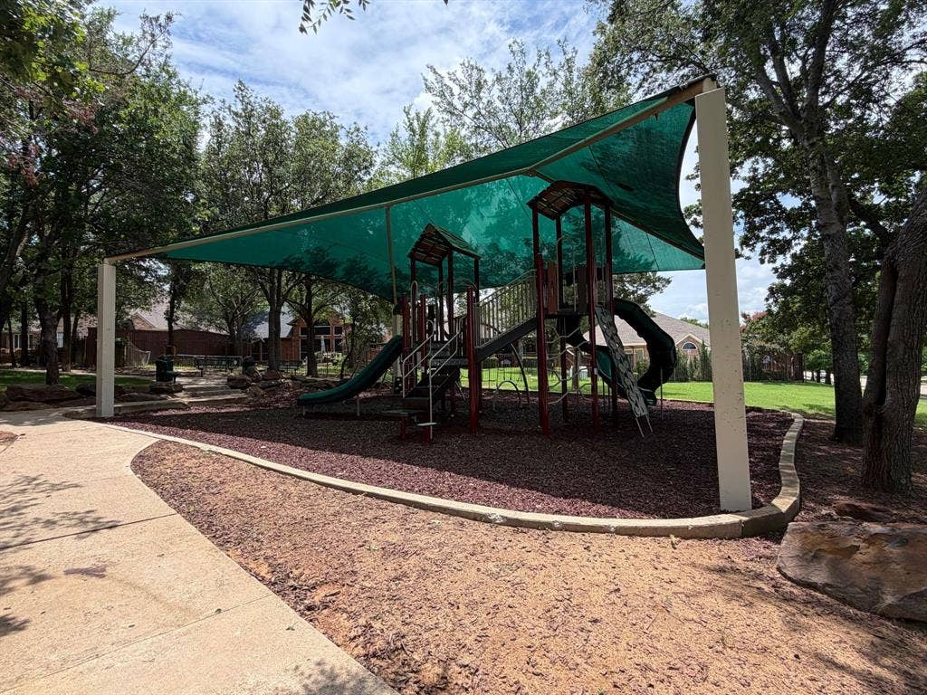 1712 Tealwood Lane, Corinth, TX 76210 Community playground featuring a multi-level structure with slides, a protective shade canopy, a wood chip surface, and a winding concrete pathway
