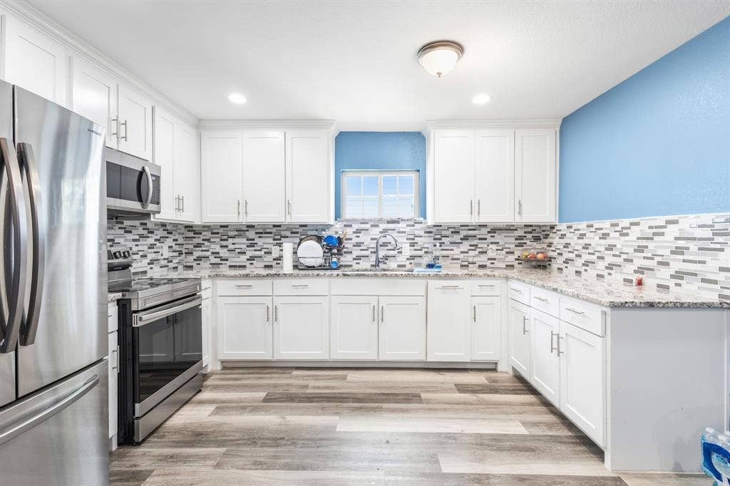 2006 Fort Worth Street, Grand Prairie, TX 75050 Bright kitchen featuring white cabinetry, stone countertops, stainless steel appliances, a mosaic tile backsplash, and wood-finish flooring