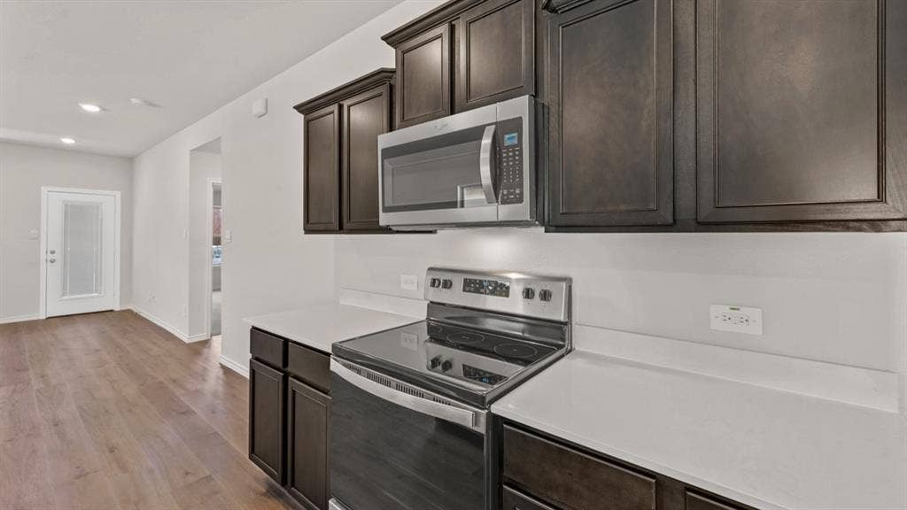 1631 Blaire Drive, Tyler, TX 75702 Kitchen area featuring dark wood-finish cabinetry, stainless steel appliances, solid surface countertops, and wood-finish flooring