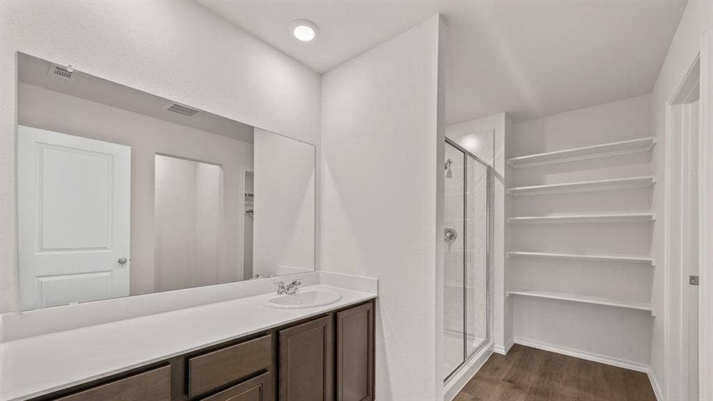 1631 Blaire Drive, Tyler, TX 75702 Bathroom featuring a single-sink vanity with white countertop, dark wood-finish cabinetry, a large wall-mounted mirror, and a glass-enclosed shower