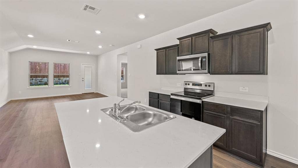 1631 Blaire Drive, Tyler, TX 75702 Kitchen island with dual basin sink and stainless steel faucet, dark wood-finish cabinetry, stainless steel microwave, stainless steel electric range, and light countertops