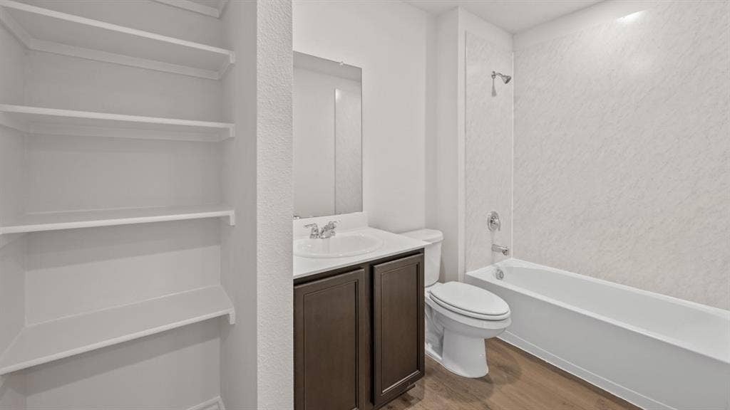 1631 Blaire Drive, Tyler, TX 75702 Bathroom with a single vanity, wood-finish flooring, a toilet, and a white tub with an integrated showerhead and textured surround
