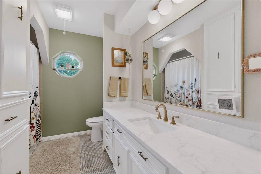 1151 Lynn Way, Waxahachie, TX 75165 Bathroom featuring an octagonal window, a large vanity with a white countertop, dual under-mount sinks, and brass-finish fixtures